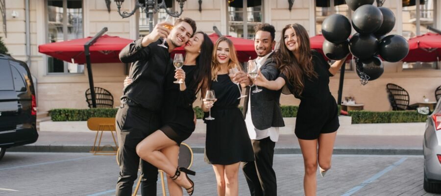 Full-length outdoor photo of happy friends having fun on double date. Pretty blonde girl in black dress posing between dancing couples on the street.